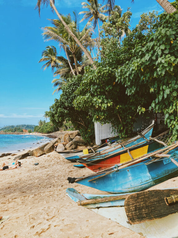 A few fishermen's boats sitting on a tropical beach with palm trees, clear water and blue sky.